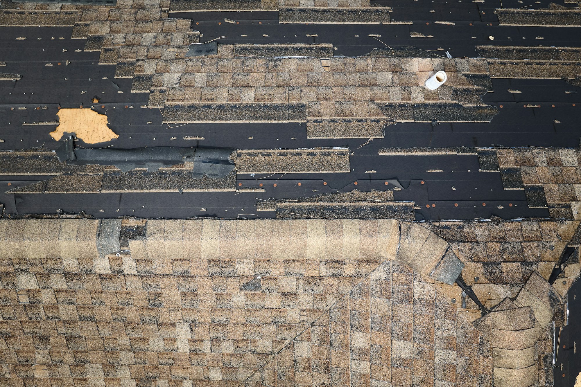 Wind damaged house roof with missing asphalt shingles after hurricane Ian in Florida.